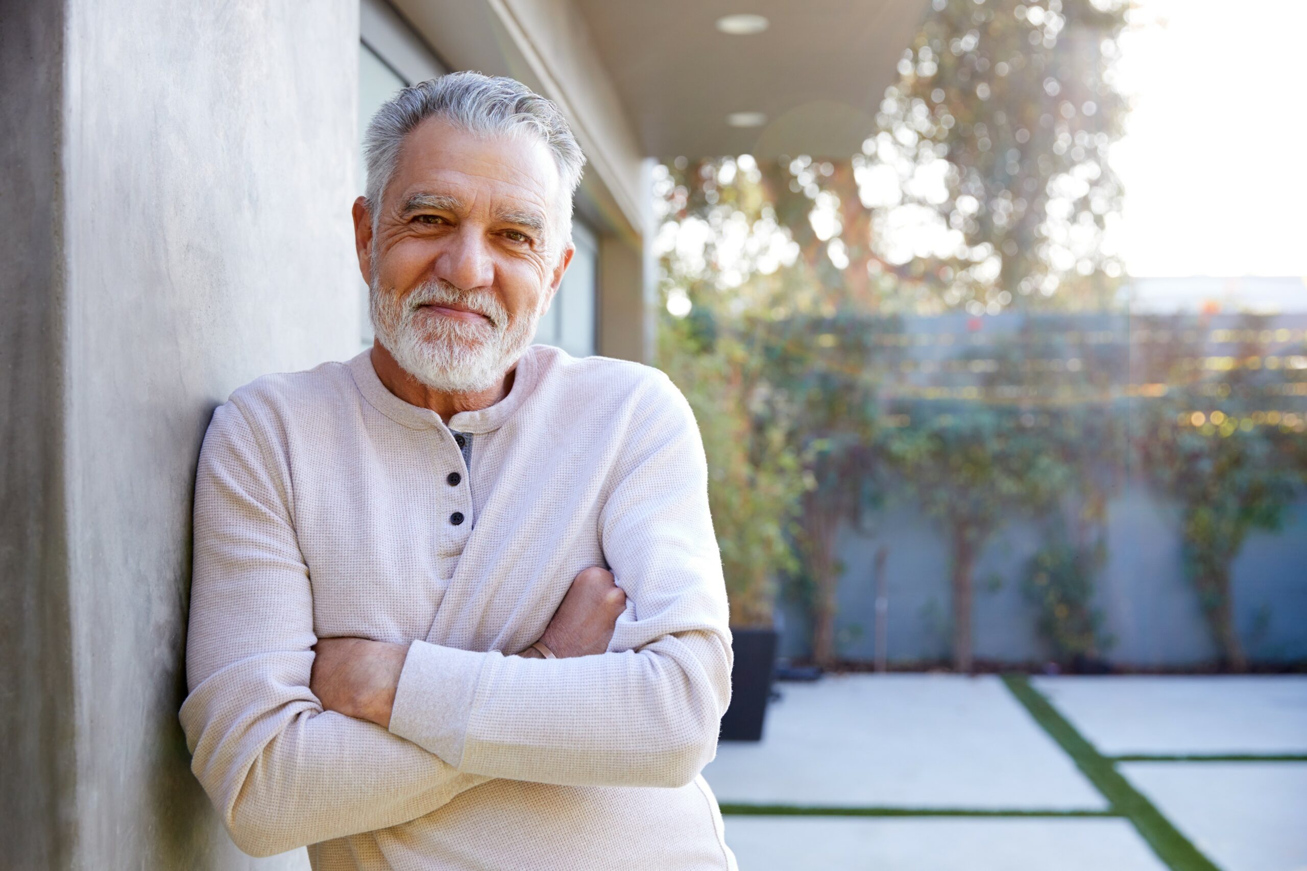 Portrait Of Smiling Retired Senior Man In Garden At Home Against Flaring Sun